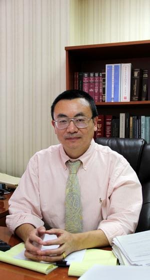 A man in glasses and a tie sitting at his desk.